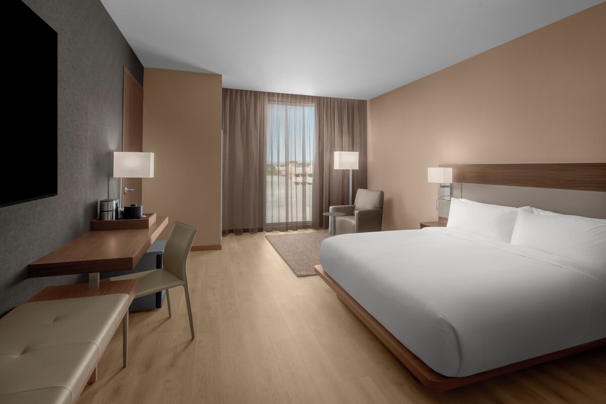 A hotel room with a bed, a desk, a chair, a TV, and a window with curtains.