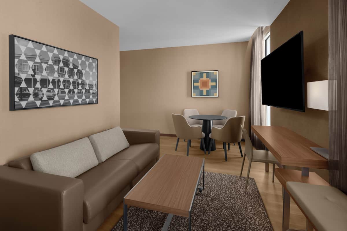 Une chambre d’hôtel moderne, équipée d’un canapé, d’une table à manger, de chaises, d’un téléviseur et ornée d’œuvres d’art sur les murs.