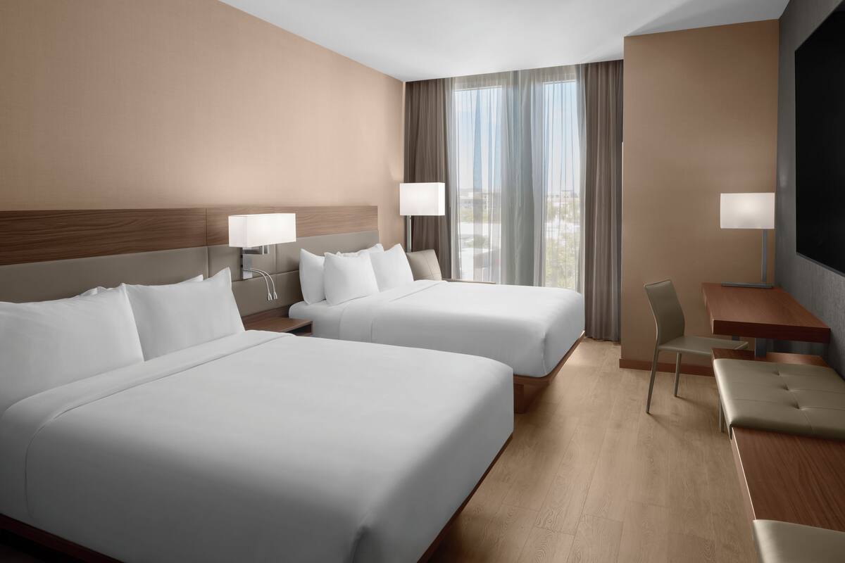 Une chambre d’hôtel avec deux lits, un bureau, une chaise et un téléviseur.