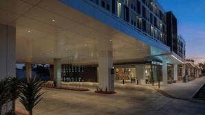 Un hotel moderno con una entrada amplia, un área de espera techada y un restaurante a la vista.
