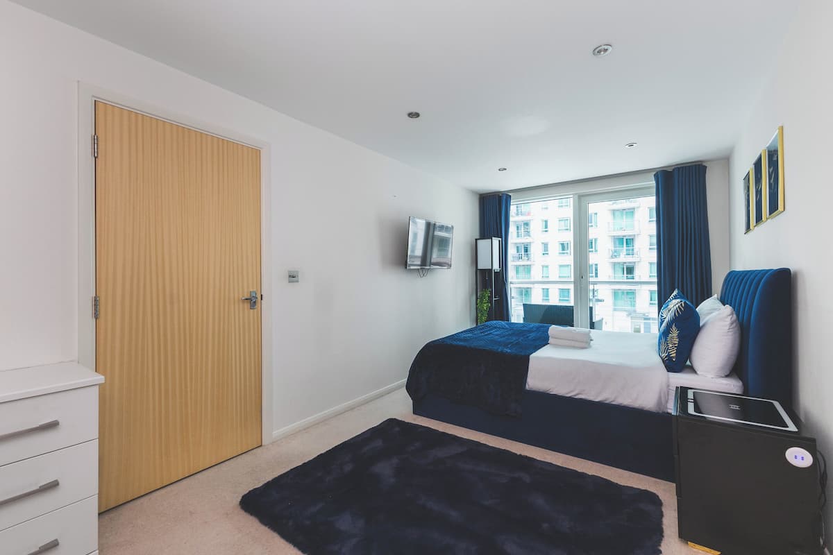 A bedroom with a bed, a TV, a desk, and a window with curtains.