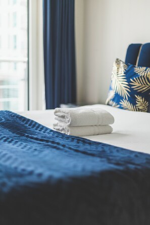 Een net opgemaakt bed met een blauwe deken en een gevouwen witte handdoek.