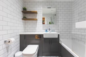 Een moderne badkamer met witte metro tegels, een witte wastafel, een toilet en een bad.