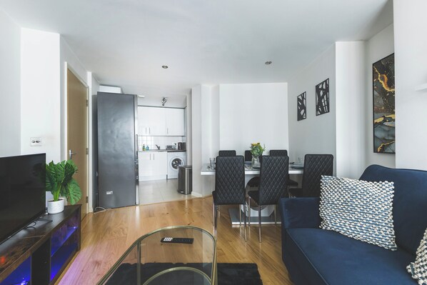 Een moderne woonkamer met een televisie, bank en eethoek.