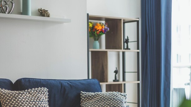 A modern living room with a dark blue sofa, patterned cushions, a glass coffee table, and a bookshelf with decorative items. - Deluxe Two-Bedroom Vauxhall Apartment (London)
