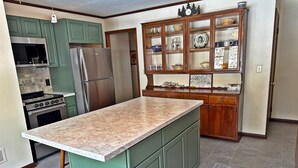 Eine Küche mit grünen Schränken, einer Marmorarbeitsplatte, einem Einbauofen, einem Kühlschrank und einer Holzauslage mit Glastüren.