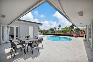 Eine überdachte Terrasse mit Pool, Gartenmöbeln und Blick auf die Nachbarhäuser.