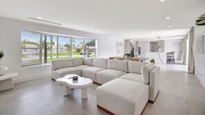 A modern living room with a sectional sofa, a small round table, and a dining area with a bar. - Intracoastal Villa | Pool + 40ft Dock | Sleeps 8 (Fort Lauderdale)