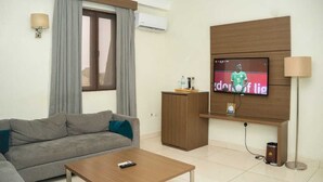 Ein modernes Wohnzimmer mit grauem Sofa, einem Holztisch, einem an der Wand befestigten Fernseher und einer kleinen Kommode.
