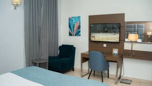 Ein Hotelzimmer mit einem Bett, einem Schreibtisch, einem Stuhl, einem Fernseher, einer Lampe und einem Bild an der Wand.
