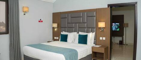 Habitación de hotel con una cama grande, dos mesitas de noche, un televisor y una puerta que da a otra habitación.