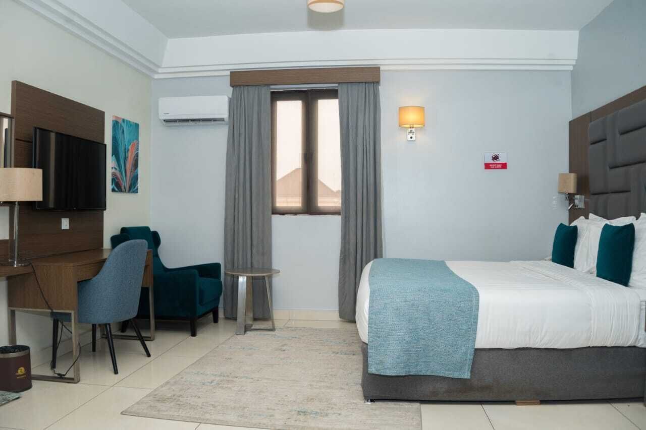 A hotel room with a bed, a desk with a chair, a TV, and a window with curtains.