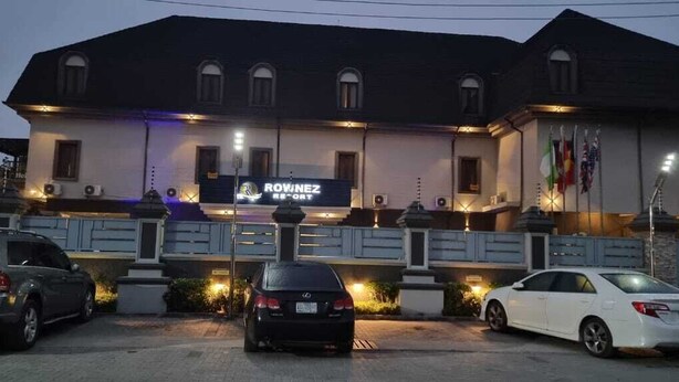 A hotel named "Rowne" with a signboard, a parking lot with cars, and a building with multiple windows and flags. - Rownez Resort  (Lagos)