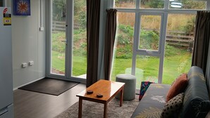 Un salón moderno con un sofá, una mesa de madera y vistas a un jardín a través de amplios ventanales.