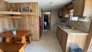 Eine kleine Küche mit Holzschränken, einem Esstisch mit Bänken, einem kleinen Kühlschrank und einer Mikrowelle.