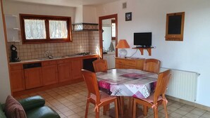 A compact kitchen with wooden cabinets, a dining table with chairs, a television, and a radiator. - Gîte de Pigneux (Saint-Genix-les-Villages)