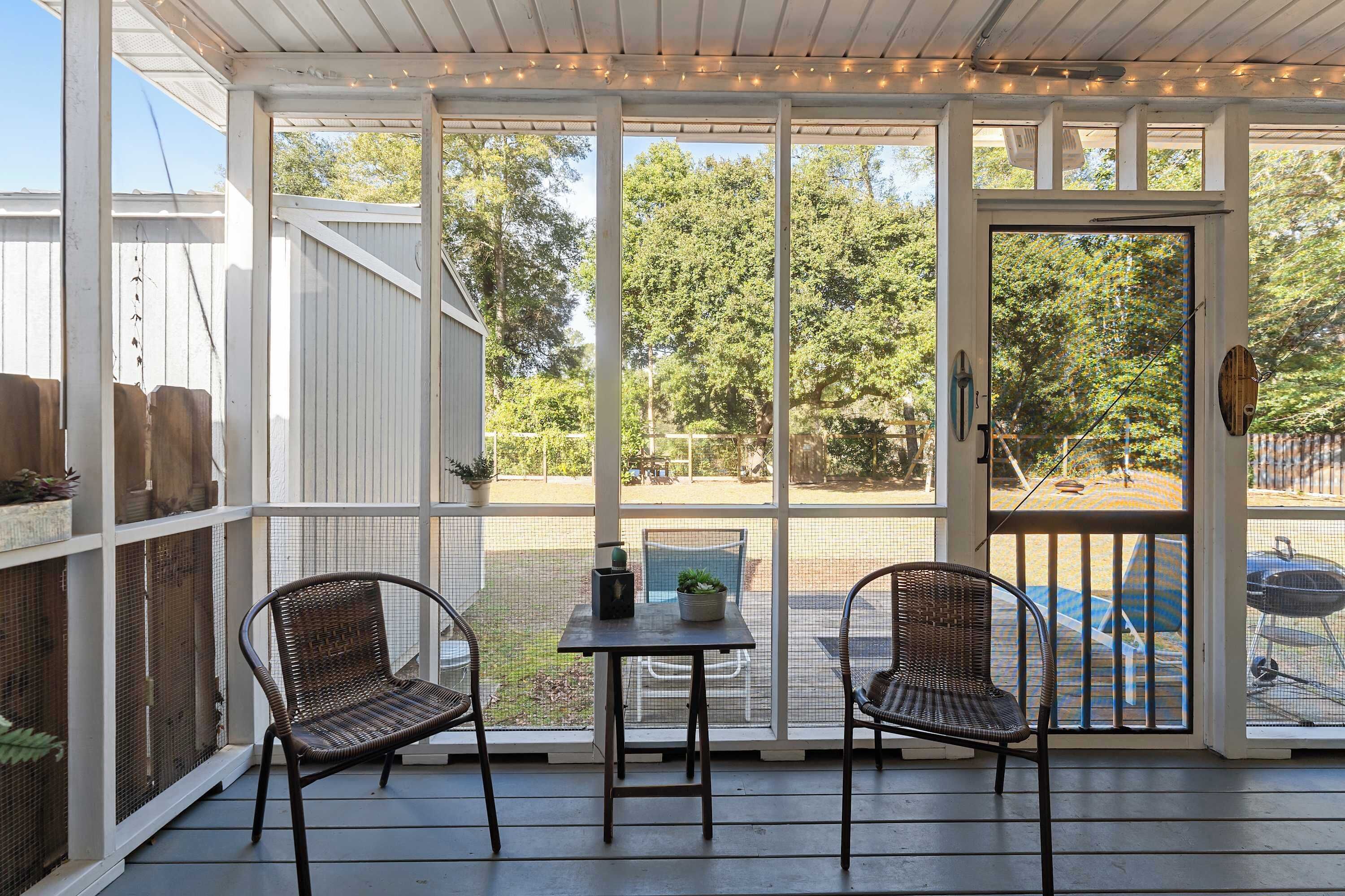 A covered patio with two wicker chairs and a small table, overlooking a backyard with a grill and a swimming pool.