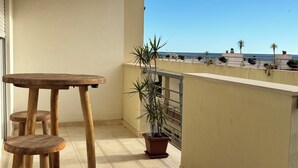 Un balcón con una mesa y taburetes de madera, una planta en maceta y vista al mar.