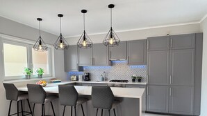 Una cocina moderna con una isla central, taburetes de bar, iluminación colgante y muebles grises.