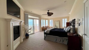 A spacious bedroom with a large bed, a ceiling fan, a TV mounted on the wall, and a view of the ocean through large windows. - Beach & Bay Views at Ocean Oasis in Brigantine! (Brigantine)