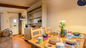 Un coin repas chaleureux avec une table en bois dressée pour le repas, agrémentée de pain, de fromage et d’un vase de fleurs.