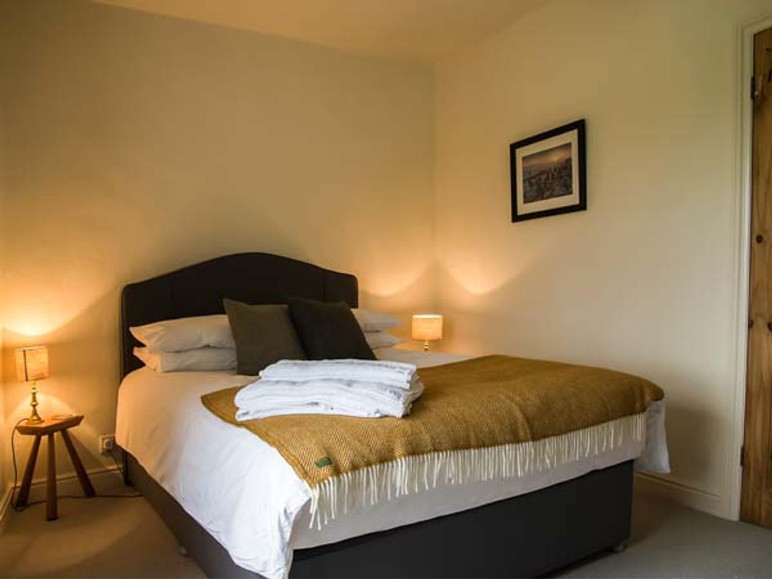 A neatly made bed with a dark headboard, white linens, and a brown throw blanket. There are two bedside lamps on either side of the bed.