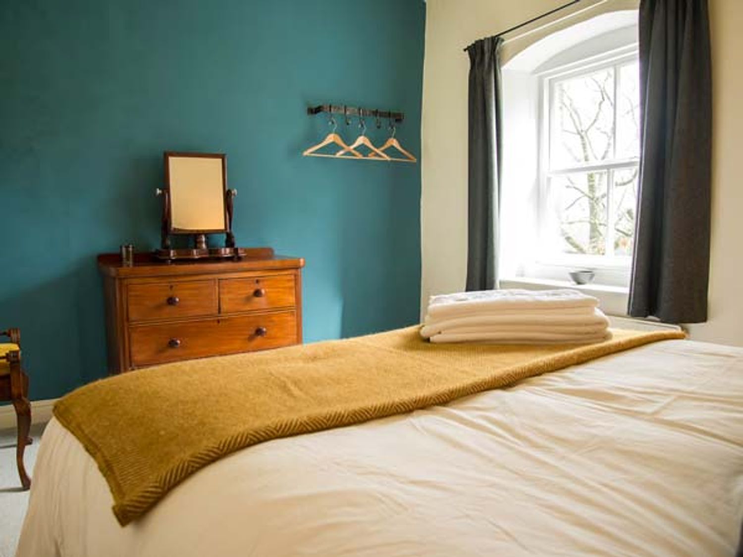 Un dormitorio con cama, cómoda, espejo y ventana con cortinas.