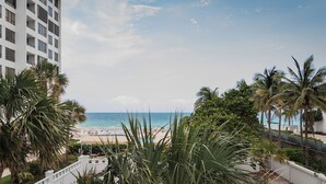 Une vue sur la plage depuis un balcon donnant sur une plage de sable, bordée de palmiers, sous un ciel dégagé.