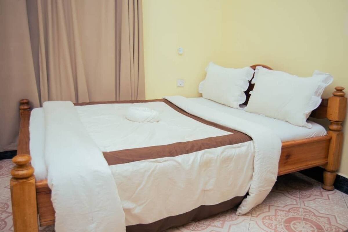 Una cama con estructura de madera, ropa de cama blanca y detalles en marrón.