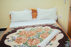 Un lit avec une couvre-lit à motifs floraux, deux oreillers blancs et une tête de lit en bois.