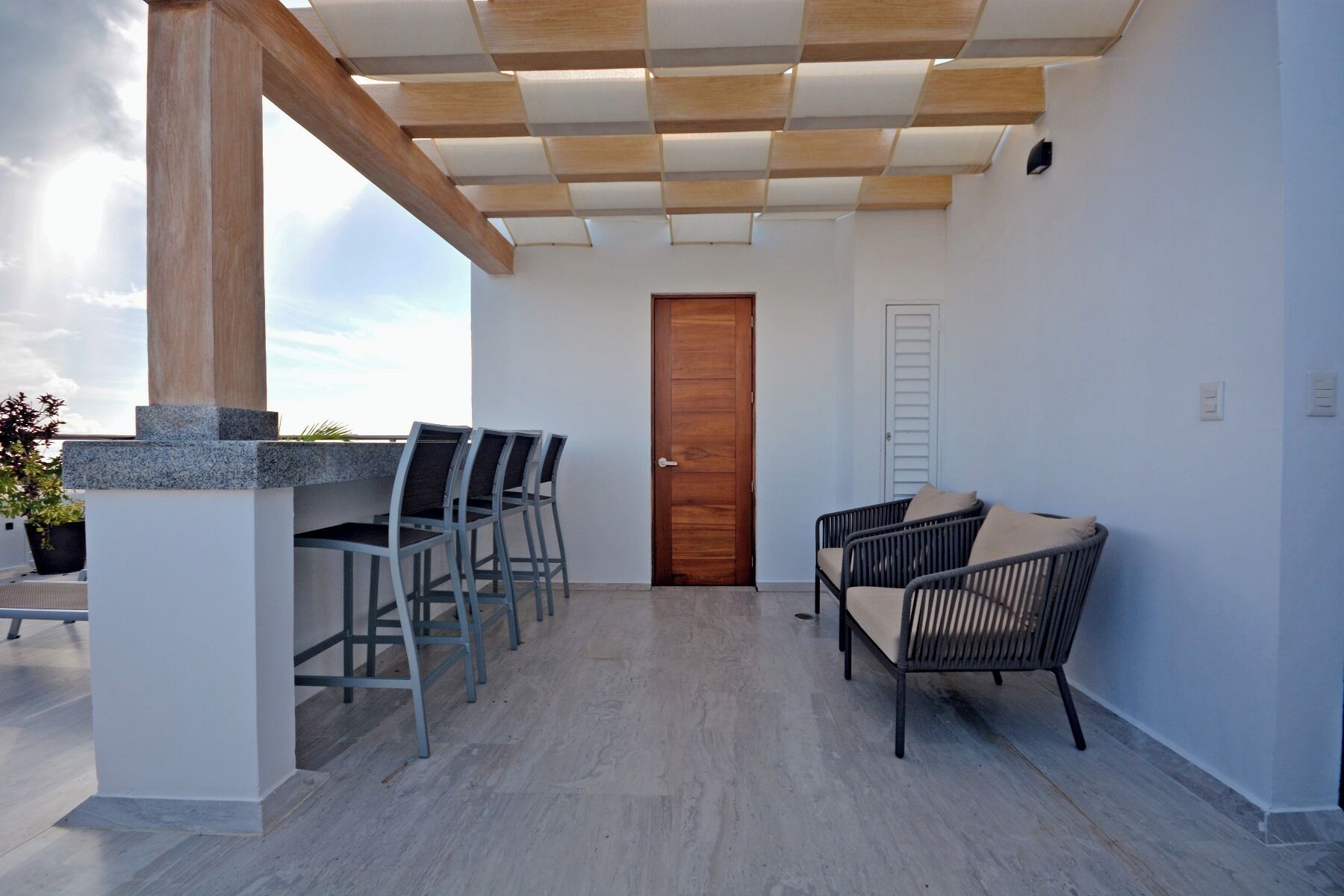 Eine überdachte Terrasse mit kariertem Himmel, einer Holztür und zwei Korbstühlen.