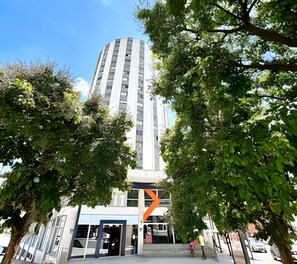 En modern byggnad med en framträdande entré, omgiven av frodiga, gröna träd.