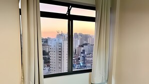 A room with a cityscape view through a window, a table with plates, and a chair. - KitiHaus Campinas (Campinas)