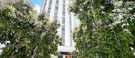 A tall building with a modern design, surrounded by trees and a clear sky.