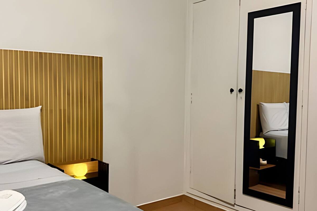 Een slaapkamer met een bed, nachtkastje, lamp, garderobe en spiegel.