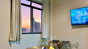 A hotel room with a bed, a small table, a chair, a TV, and a window with curtains. - KitiHaus Campinas (Campinas)