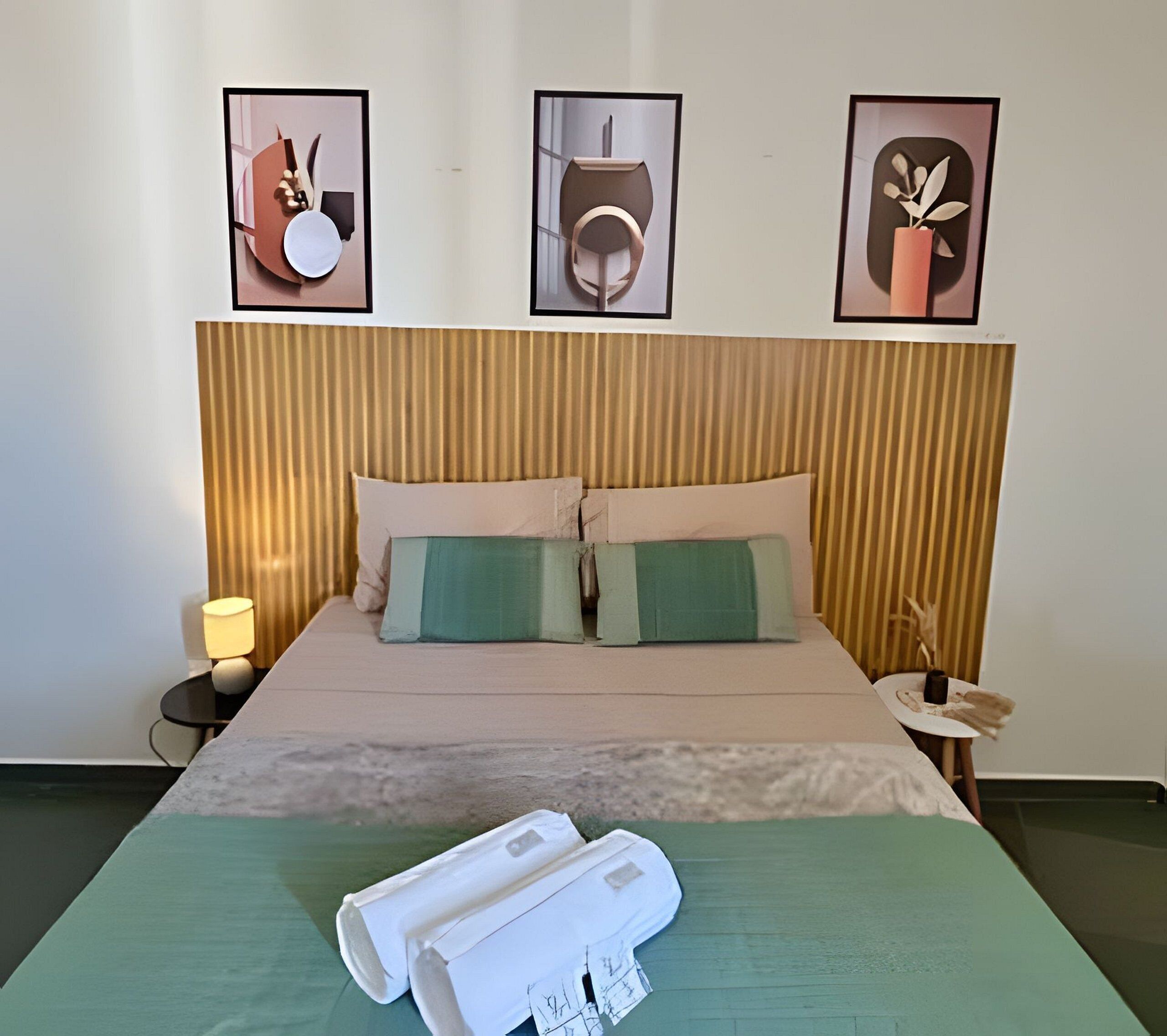 A hotel room with a bed, pillows, a nightstand, a lamp, and framed pictures on the wall.