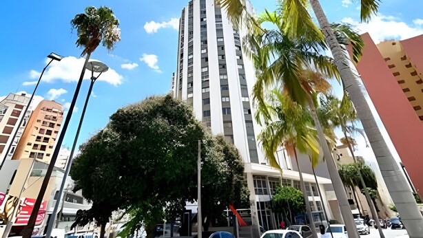 A tall building with a modern design, surrounded by palm trees and parked cars. - KitiHaus Campinas (Campinas)