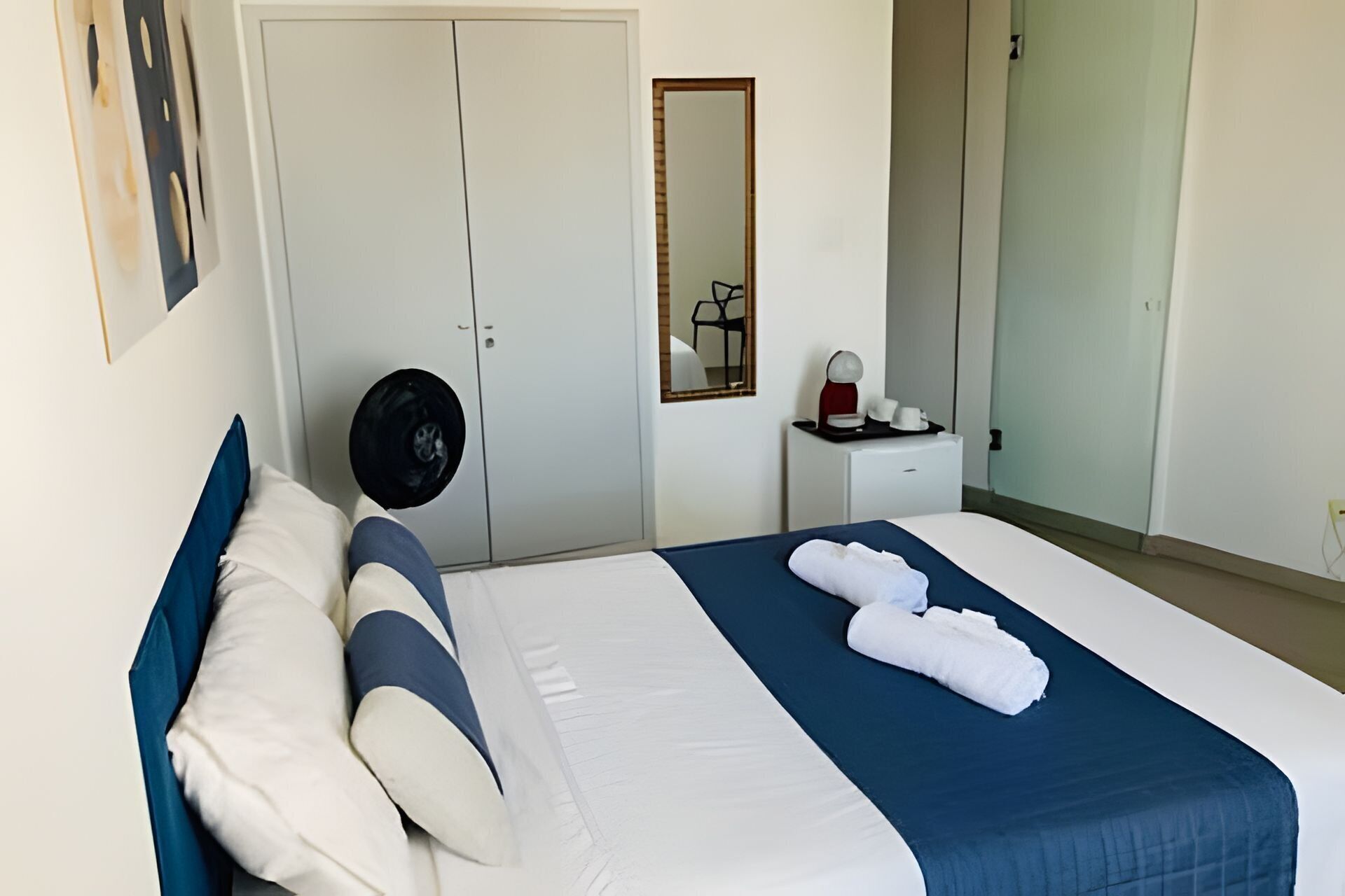 Habitación de hotel con cama, mesita de noche con lámpara, espejo y armario.