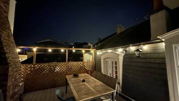 Une terrasse avec une table et des chaises, une clôture en bois et des guirlandes lumineuses.