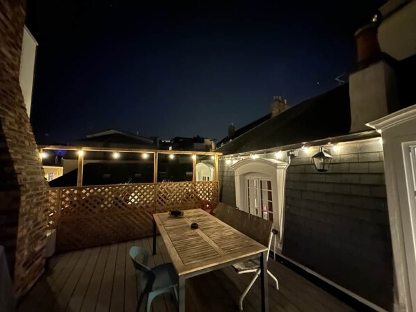 A patio with a table and chairs, a wooden fence, and string lights.