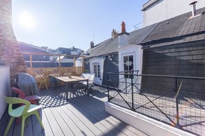 Une terrasse sur le toit, avec une table et des chaises, un barbecue abrité et une vue sur les bâtiments voisins.