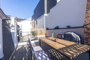 A wooden deck with a table and chairs, a barbecue grill, and a small garden area with a fence and potted plants. - Villa Barillerie 1870 - Centre - 24 personnes (Le Mans)
