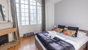 Un dormitorio con cama, mesita de noche, ventana con cortinas y chimenea.