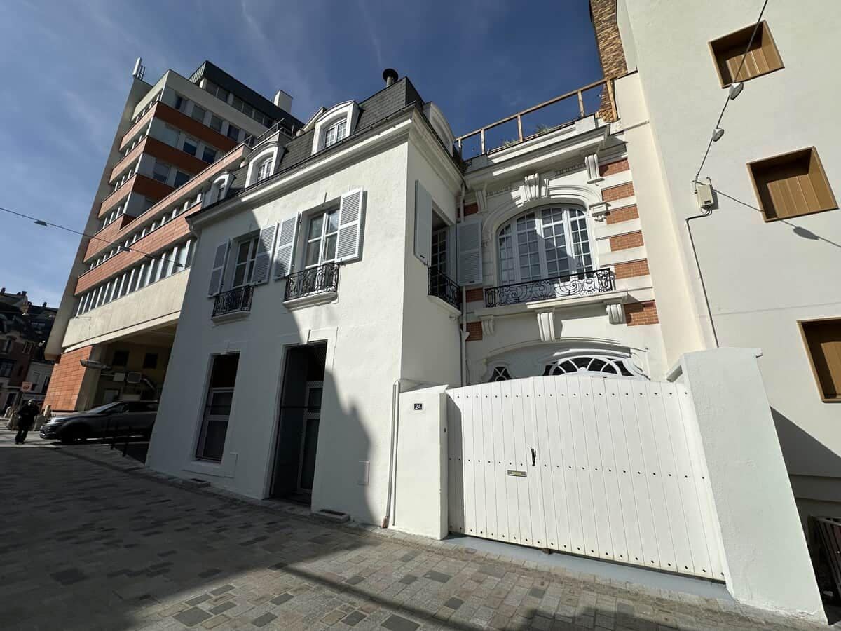 Un immeuble à plusieurs étages, doté d’une façade blanche, d’une entrée fermée par un portail et d’un balcon orné de balustrades en fer forgé.