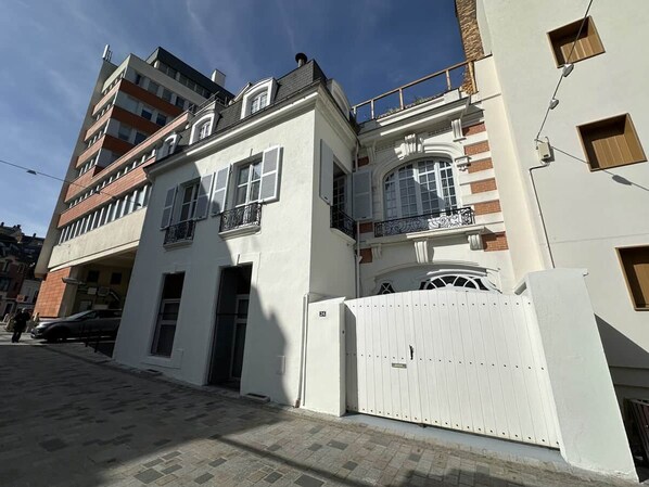 A multi-story building with a white facade, a gated entrance, and a balcony with wrought iron railings.