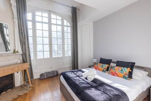 A bedroom with a bed, a bedside table, a window with curtains, and a fireplace.