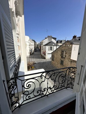 A narrow street with buildings on either side, a clear blue sky, and a balcony with ornate black metal railings. - Villa Barillerie 1870 - Centre - 24 personnes (Le Mans)