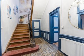Un escalier recouvert d’une moquette rouge, avec des murs bleus et un radiateur blanc.