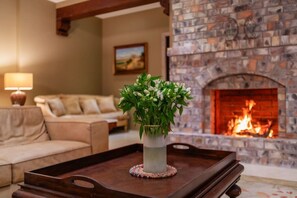 A living room with a stone fireplace, a beige sofa, and a vase with flowers on a wooden tray.
